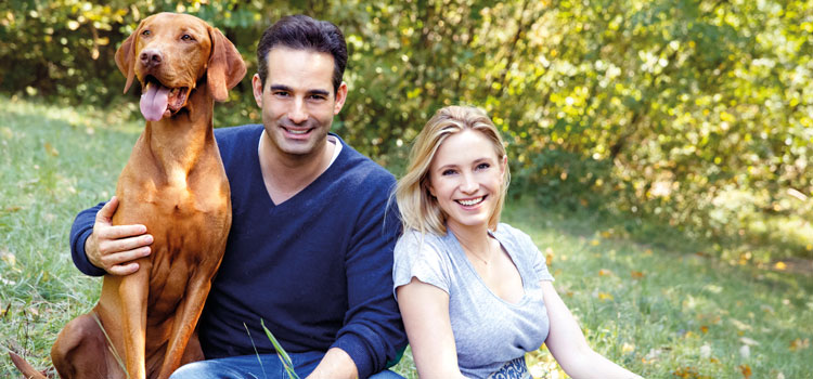 Katharina und Stefan Miklauz wie sie mit ihrem Hund Pluto auf einer Wiese sitzen.